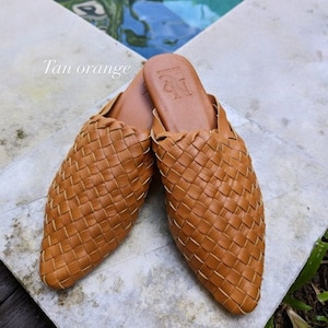 K&ouml;nnte beinhalten: Tan-orangefarbene geflochtene Leder-Mules mit spitzer Zehenpartie. Die Schuhe haben ein schlichtes Design und sind aus hochwertigem Leder gefertigt. Der Markenname "N" ist auf der Oberseite des Schuhs gepr&auml;gt.