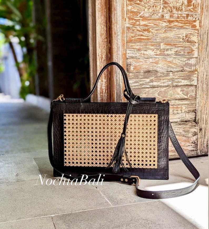 May include: A black leather tote bag with a woven rattan panel and a long strap. The bag has a gold zipper and a tassel.
