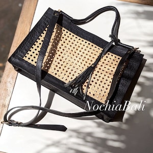 May include: A black leather tote bag with a woven rattan panel and a long tassel. The bag has a top handle and a long shoulder strap. The bag is made by Nochia Bali.