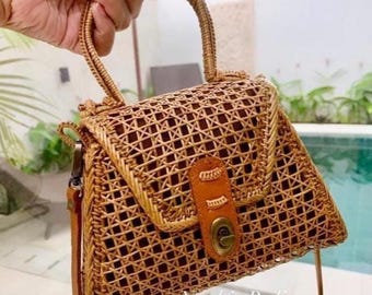 May include: A woven brown rattan handbag with a top handle and a long shoulder strap. The bag has a flap closure with a metal clasp and a leather accent.