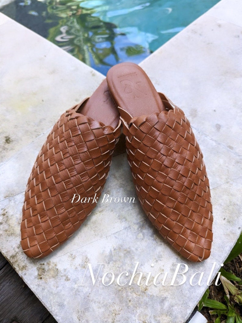 K&ouml;nnte beinhalten: Ein Paar dunkelbraune, geflochtene Lederschlappen. Die Schlappen haben eine spitze Zehenpartie und ein geflochtenes Design. Der Text "Dark Brown" und "N ochia Bali" ist im Bild zu sehen.