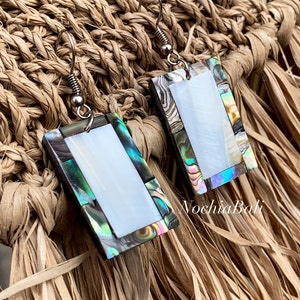 May include: A pair of iridescent rectangular earrings with a white mother of pearl center. The earrings are made of abalone shell and have silver hooks.
