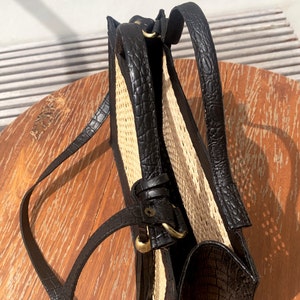 May include: A black leather handbag with a woven straw panel and a long shoulder strap. The bag has a gold buckle and a flap closure.