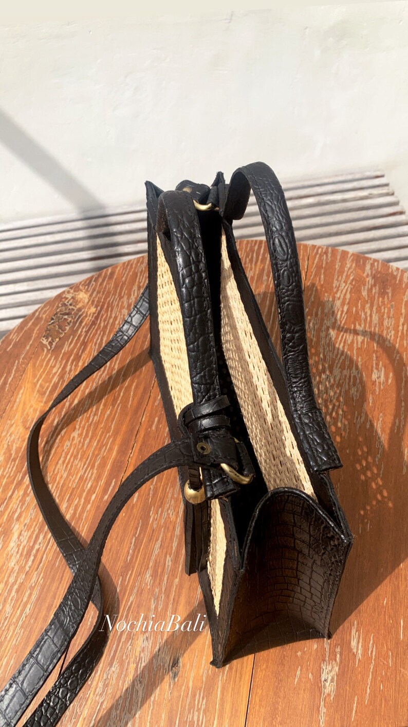May include: A black leather handbag with a woven straw panel and a long shoulder strap. The bag has a gold buckle and a flap closure.