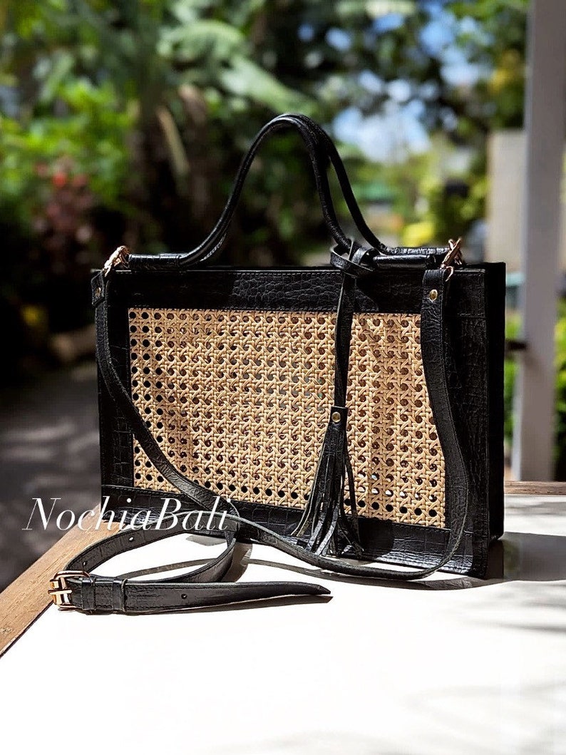 May include: A black leather tote bag with a woven rattan panel and a tassel. The bag has a top handle and a detachable shoulder strap.