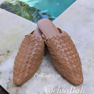 K&ouml;nnte beinhalten: Ein Paar geflochtene Lederslipper in Tan mit spitzer Zehenpartie. Die Schuhe befinden sich auf einer hellfarbigen Oberfl&auml;che mit dem Text "Pull up tan" und "NochlaBali" darunter.