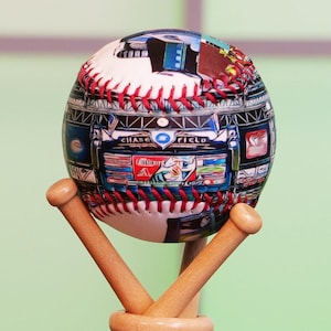 May include: A baseball with a colorful design featuring a baseball field and the words "Chase Field". The baseball is on a wooden stand with two bats.