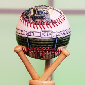 May include: A baseball with a colorful image of a building and the text "Truist Park" on it. The baseball is on a wooden stand with two bats.