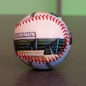 May include: White baseball with red stitching and a colorful image of a baseball park with the word "PARK" printed on the side.