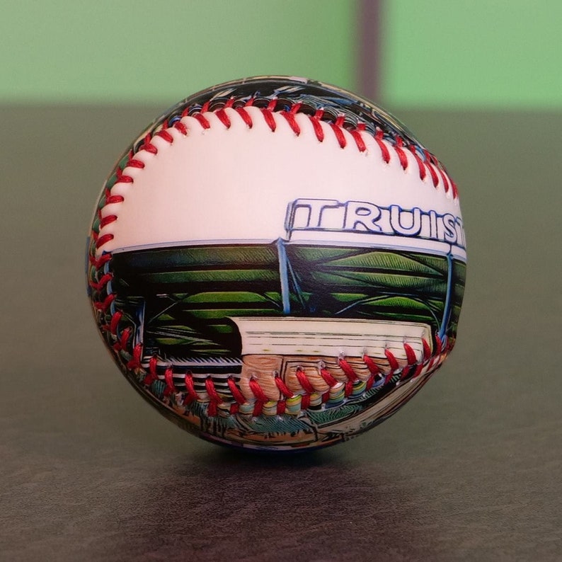 May include: A white baseball with red stitching and a printed image of a baseball stadium with the word "TRUIST" on the side.