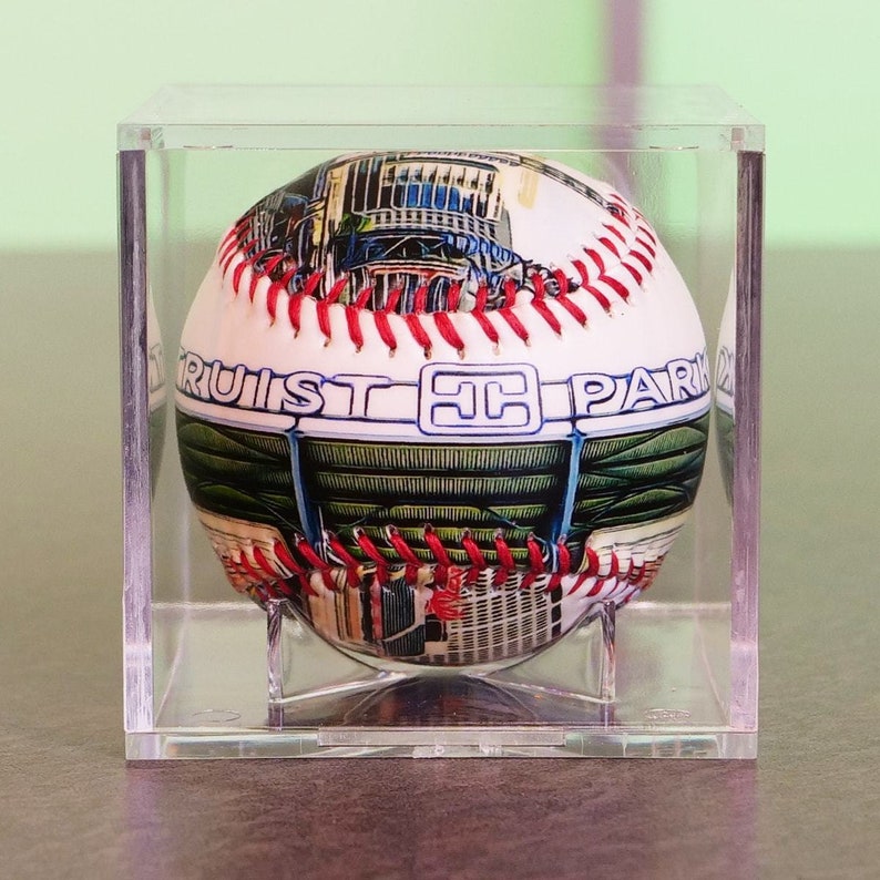 May include: A white baseball with red stitching and a colorful image of a baseball stadium. The baseball has the text "Truist Park" printed on it.