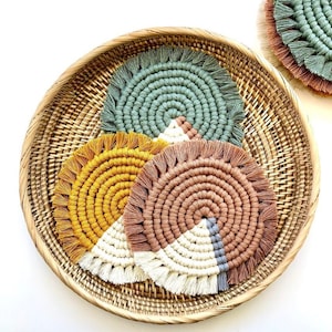 May include: Four round woven macrame coasters in a wicker basket. The coasters are in shades of green, yellow, brown, and white.