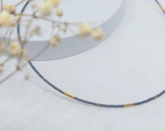 May include: A delicate choker necklace made with small gray beads and gold accents.