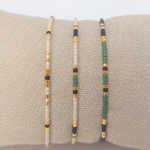 May include: Three beaded bracelets featuring a white, black and green colour scheme. The bracelets are crafted with small, round beads and have a simple, minimalist design.