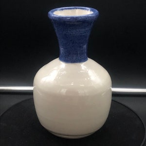May include: A white ceramic vase with a blue rim. The vase has a round body and a narrow neck.