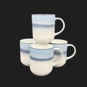 May include: Four ceramic mugs stacked together. The mugs have a white base, a light blue band, and a light blue top. Each mug has a white handle. The mugs are suitable for hot drinks.