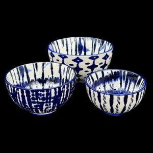 May include: Set of three ceramic bowls with a white and blue abstract pattern. The bowls vary in size and feature a dark blue rim and interior design. The bowls are suitable for serving food.