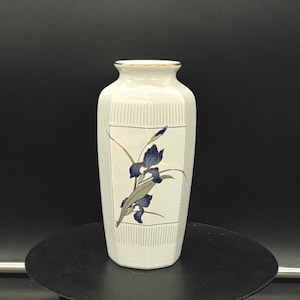 May include: White ceramic vase with a gold rim and a blue and gold floral design. The vase has a rectangular shape and a striped pattern.