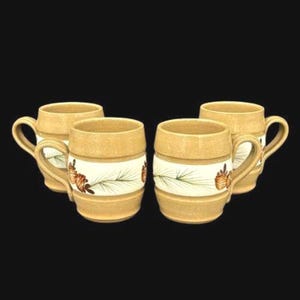Könnte beinhalten: Ein Set aus drei Keramikbechern mit gesprenkelter, matter Oberfläche. Die Becher sind in den Farben Creme, Hellgrau und Dunkelgrau gehalten. Jeder Becher hat ein schlichtes, modernes Design und einen abgerundeten Henkel.