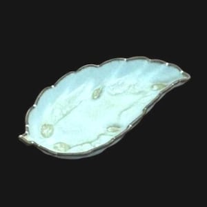 Pode incluir: Um prato decorativo em forma de folha com um interior azul claro e branco marmoreado e uma borda prateada com vieiras. O prato tem alguns pequenos detalhes dourados. O fundo é preto.