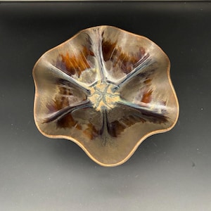 May include: A brown and grey ceramic bowl with a wavy, flower-like rim. The bowl has a dark brown glaze with streaks of lighter brown and grey.