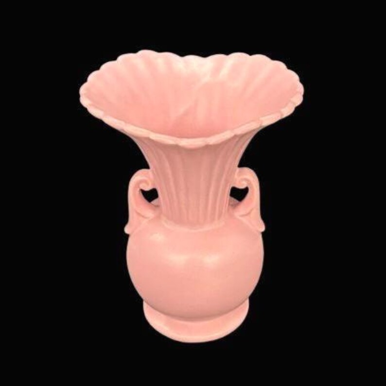 May include: A pink ceramic vase with a ruffled rim and two small handles. The vase has a bulbous base and a flared, ribbed neck. The overall design is symmetrical and the vase is set against a black background.