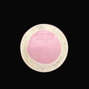 May include: A round, ceramic object with a pink center and a cream-colored rim. The center has a slightly raised texture and the letters "USA" are visible. The object is set against a black background.