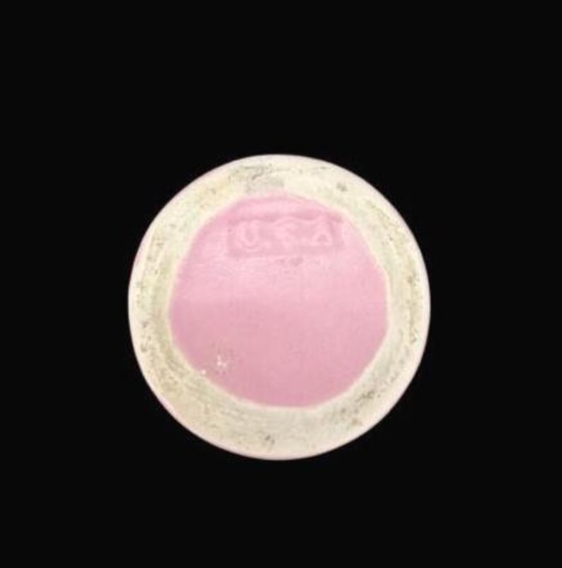 May include: A round, ceramic object with a pink center and a cream-colored rim. The center has a slightly raised texture and the letters "USA" are visible. The object is set against a black background.