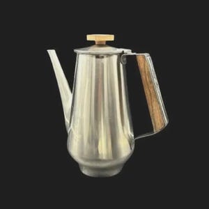 May include: A white ceramic mug with a black handle and the text "But First, Coffee" in a bold, black font. The mug is set against a blurred background, suggesting a cosy setting.