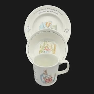 May include: A three-piece children's dish set featuring illustrations and text from a classic children's story. The set includes a plate, a bowl, and a mug, all with a white background and colorful drawings.