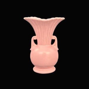 May include: A pink ceramic vase with a flared, ruffled top and two curved handles. The vase has a bulbous body and a round base. The fluted design on the top adds a decorative touch. The vase is a soft, muted pink color.