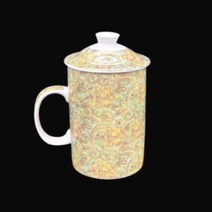May include: A ceramic mug with a lid, featuring a floral pattern in yellow and green. The mug has a white handle and a white lid. The design is reminiscent of vintage teacups. The mug is suitable for hot beverages.