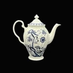 Puede incluir: Tetera de cerámica color crema con tapa, con un diseño floral azul. La tetera tiene un asa curva y un pico. El patrón floral incluye flores y hojas estilizadas. La tetera es probablemente para servir té.