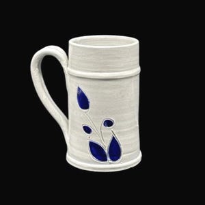 May include: A white ceramic mug with a handle and a cylindrical body. The mug features a blue floral design on the front. The mug is suitable for hot or cold beverages.