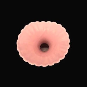 May include: A light pink, donut-shaped vase with a scalloped edge. The vase has a central opening and a smooth, matte finish. The background is solid black.