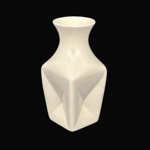 May include: Ivory-colored ceramic vase with a geometric, faceted design. The vase has a square base that tapers to a flared neck. The surface is smooth and glossy, reflecting light. A decorative piece for home decor.