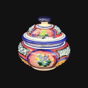 May include: A hand-painted ceramic jar with a lid. The jar features a vibrant design with red, blue, and yellow accents. Floral patterns and geometric shapes adorn the surface, creating a decorative and colorful piece.