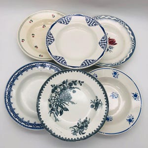 Può includere: Una collezione di sei piatti antichi in ceramica con vari motivi decorativi. I piatti presentano disegni in blu, rosso e verde, tra cui motivi floreali, geometrici e bordi dettagliati. I piatti sono disposti su una superficie bianca.