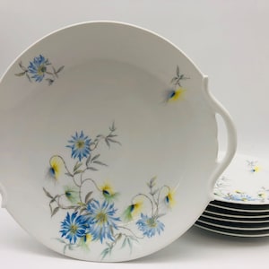 Può includere: Un set di piatti in porcellana bianca con un motivo floreale con fiori blu e gialli. I piatti hanno bordi a festoni e due manici.