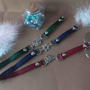Peut inclure: Trois colliers en ruban de satin avec des breloques en métal argenté. Les breloques comprennent un nœud celtique, une étoile de David et un autre nœud celtique. Les colliers sont en vert, bleu et bordeaux.