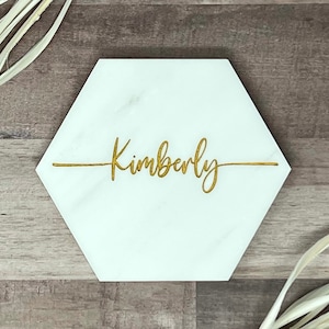 May include: White hexagonal marble coaster with the name Kimberly engraved in gold lettering.