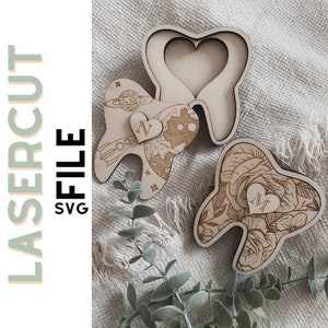 Op de afbeelding: Houten lasergesneden tandvormige decoraties met gegraveerde ontwerpen. Eén heeft een raket en planeten, een ander bloemmotieven en de derde een hartvormige uitsparing. De tekst "LASERCUT FILE SVG" staat links.