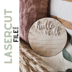 May include: A round wooden sign with the words "hallo welt" in white script. The sign has engraved leaf designs and space to write baby's name, date, weight, and height. The words "LASERCUT FILE SVG" are on the left side.