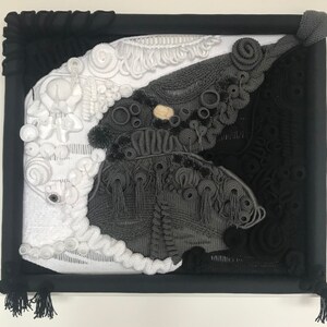 Puede incluir: Una obra de arte enmarcada en negro con un diseño abstracto blanco y gris. El diseño está hecho de tela tejida y tiene un efecto 3D.