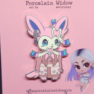 May include: A pink enamel pin featuring a Sylveon-inspired character in a kimono. The pin has a bow, floral accents, and the text "Porcelain Widow" and "seviyummy". The character has large, expressive eyes.