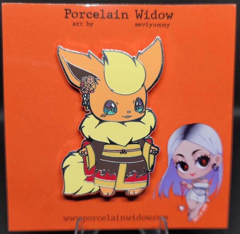 May include: A colorful enamel pin featuring an orange and yellow cartoon character with a kimono. The pin is on an orange backing card with the text "Porcelain Widow" and "seviyummy". A second cartoon character is also on the card.