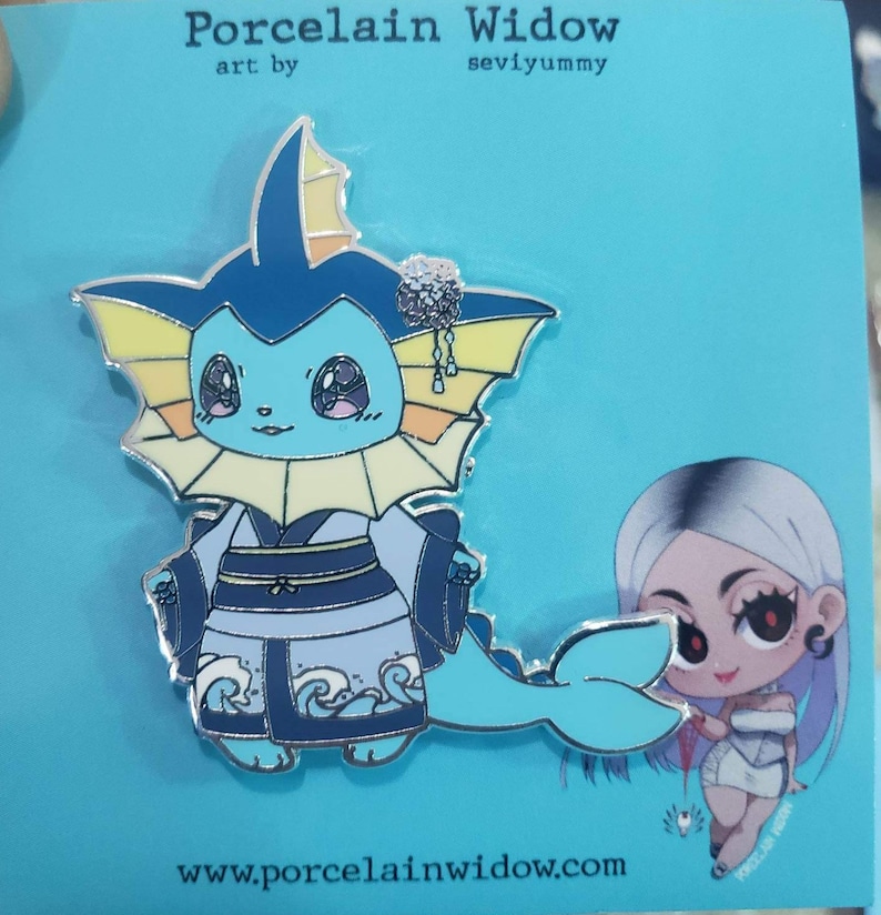 May include: A teal and silver enamel pin featuring a cartoon character in a kimono. The pin has a light blue body, dark blue kimono, and yellow accents. The pin is on a blue background with the text "Porcelain Widow" and "seviyummy".