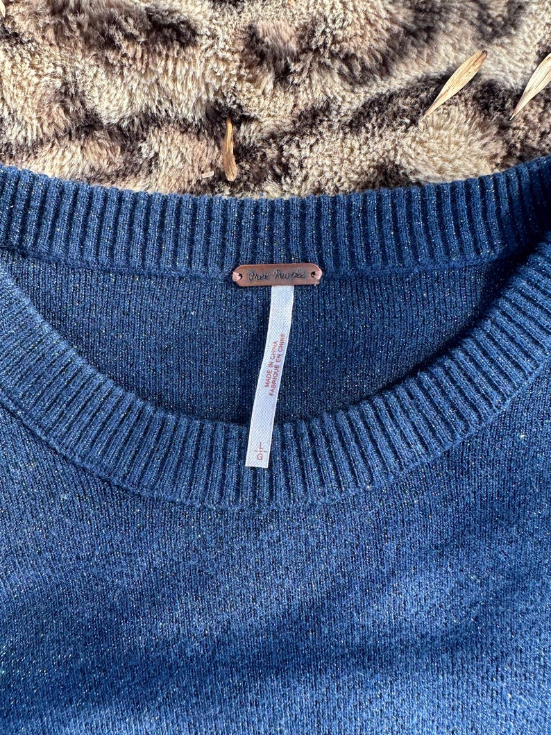 Puede incluir: Un su&eacute;ter azul oscuro con una etiqueta de Free People. La etiqueta est&aacute; unida al su&eacute;ter con un peque&ntilde;o alfiler. El su&eacute;ter est&aacute; hecho de una tela suave y de punto.