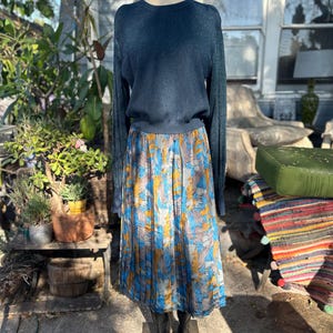 Puede incluir: Un suéter azul teal de manga larga con una falda plisada con un estampado floral azul, amarillo y marrón.
