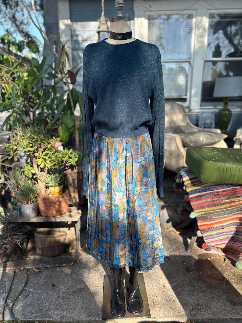 Puede incluir: Un su&eacute;ter azul teal de manga larga con una falda plisada con un estampado floral azul, amarillo y marr&oacute;n.